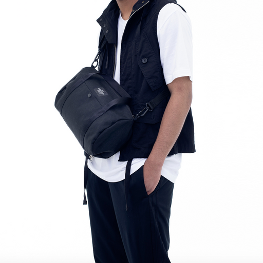 Model wearing black canvas duffle bag with shoulder strap 