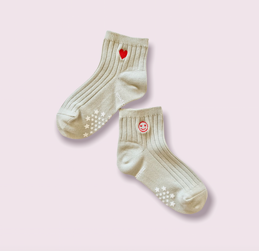 A pair of ribbed khaki colored childrens socks with an embroidered red heart and smiley face emoji at ankle & star shaped tread on bottom