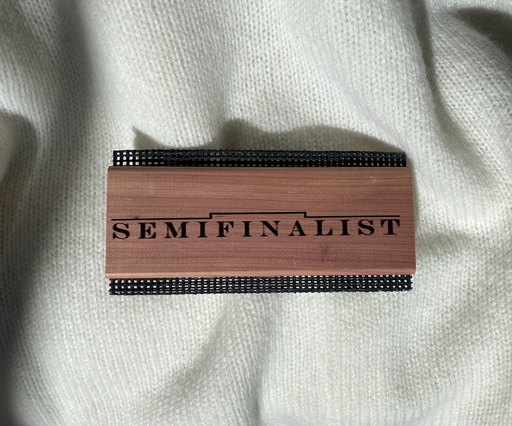 Semifinalist logo on the wooden handle of a sweater comb, sitting atop a white sweater