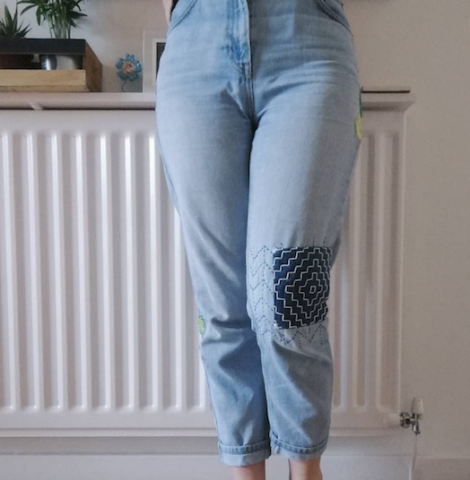 Model wearing denim pants with hand sewn knee patch