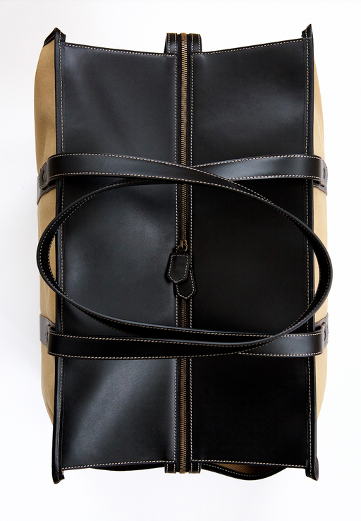 Top zipper view of tan travel bag with black leather straps