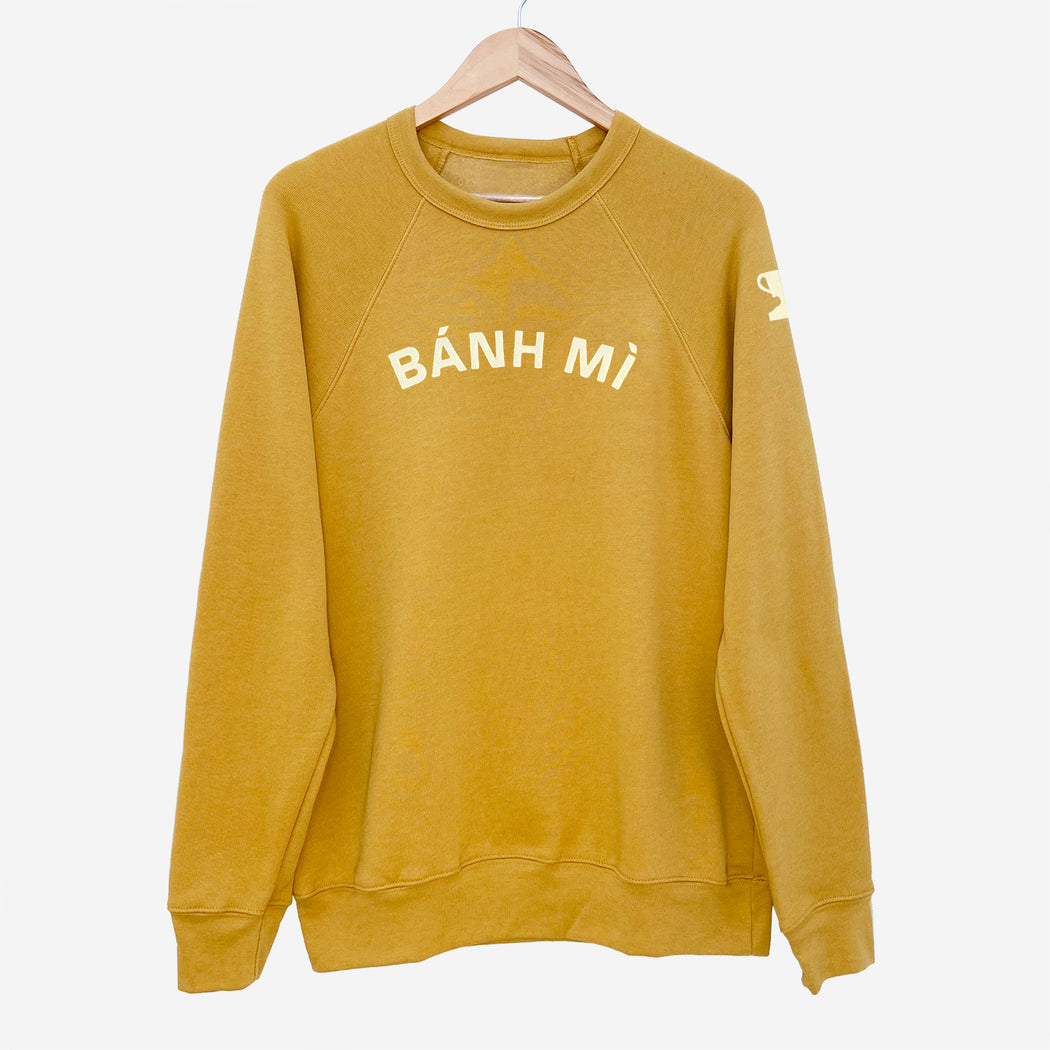 Mustard colored long sleeve sweatshirt with appliqué reading "BÁNH MI" on front