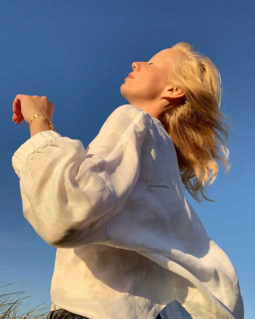 Female model wearing white button down shirt with long sleeves against a blue sky